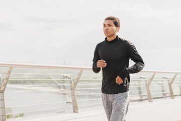 Healthy fit sporty young mixed-race african athlete sportsman in fitness outfit jogging running on city urban bridge in the morning. Shaping activity, slimming exercises.