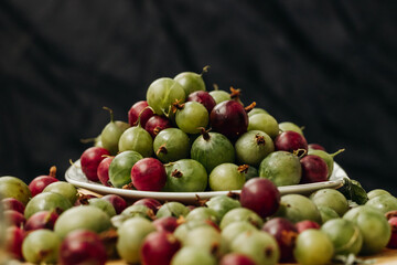Gooseberry. Green and red gooseberry berries on a black background. Gooseberries on a white plate on a black background