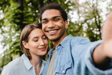 Cheerful happy young romantic couple spending time together on romantic date taking selfie on smartphone in city park. Friends boyfriend and girlfriend students taking photo outdoors.