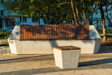 A modern concrete bench and a concrete pouf covered with brown wooden slats in a city park.
