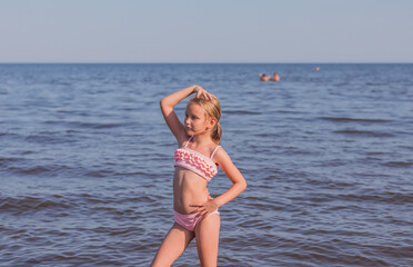 Fototapeta na wymiar girl 6-7 years old, blonde, stands in a swimsuit against the background of the sea