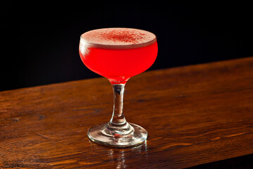Red cocktail on bar counter. Drink with martini, gin, rum, tequila and fruit on the background of bottles with alcohol. Glass with booze on a wooden board.