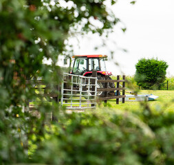 Fototapeta na wymiar Tractor in field with foreground cloudy afternoon bushes trees
