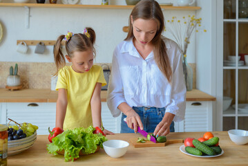 Happy mom teaches little daughter to cook healthy food, mom and girl talking, smiling, doing useful activities in the kitchen