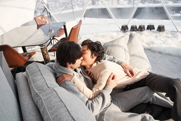 Woman and a unshaven man kissing while laying at the sofa at home