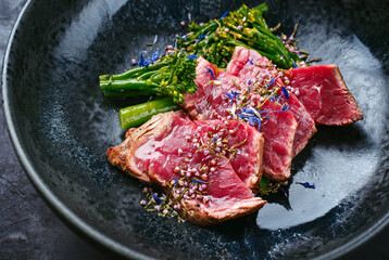 Modern style baby broccoli with fried dry aged sliced beef fillet steak served as close-up on a...
