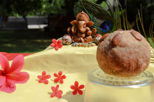 Beautiful lord Ganesha idol worshipped during Ganesh chaturthi festival with peacock feather in background. Sitting Ganpati with pillows and bolsters during Vinayaka chavithi with Ladoo in front
