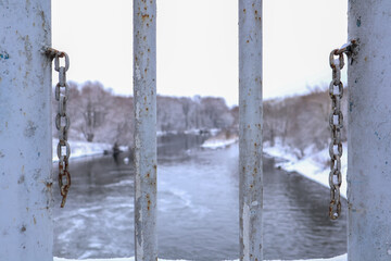view of the river through a metal fence with chains on a winter cloudy day