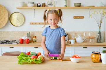 Adorable child is cooking in the kitchen. Pretty pretty girl prepares soup. Little chef preparing healthy food vegetable salad