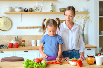 Happy mom teaches little daughter to cook healthy food, mom and girl talking, smiling, doing useful activities in the kitchen