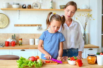 Happy mom teaches little daughter to cook healthy food, mom and girl talking, smiling, doing useful activities in the kitchen