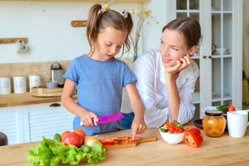 Happy mom teaches little daughter to cook healthy food, mom and girl talking, smiling, doing useful activities in the kitchen