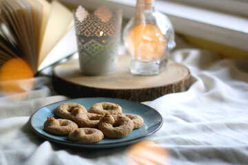 Plate with cookies, open book, lit candles and fairy lights. Hygge at home. Selective focus.