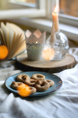 Plate with cookies, open book, lit candles and fairy lights. Hygge at home. Selective focus.