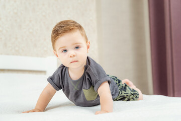Fototapeta premium Cute little baby boy lies on a bed and looking at camera. Beautiful baby boy with big blue eyes