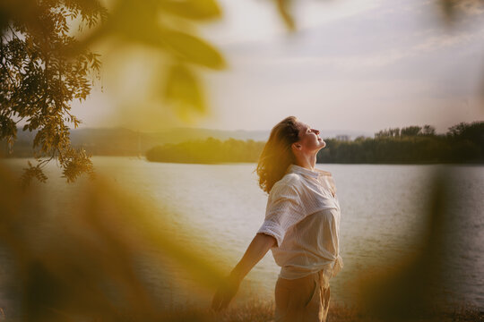 Beautiful young relaxed woman in white blouse enjoying nature breathing fresh air meditating on the river on an autumn day