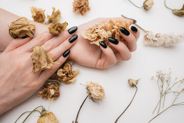 Black manicure on female hands. Hands are decorated with dried flowers. Image in beige autumn colors.