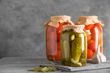 Homemade pickled tomatoes and cucumbers. Canned vegetables in glass jars on gray table. Copy space....