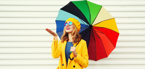 Autumn portrait of happy cheerful smiling young woman with colorful umbrella wearing a yellow coat and beret on a white background