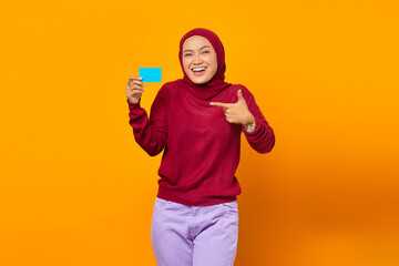 Smiling Asian woman show gesturing finger blank card over yellow background