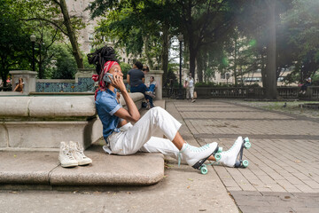 Young woman with roller skates sitting in park, talking on smart phone
