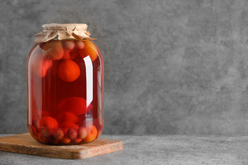 Homemade canned fruits plum and cherry compote in large glass jars on gray table. Copy space.