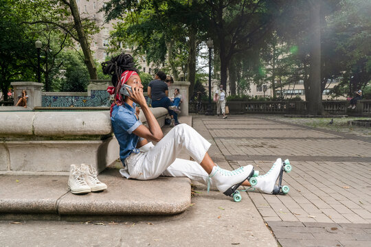 Young woman with roller skates sitting in park, talking on smart phone - Powered by Adobe