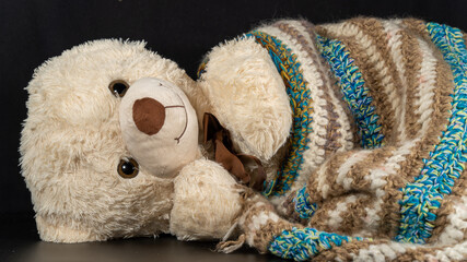 Soft toy white teddy bear wrapped in a knitted blanket, lying to sleep