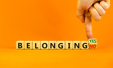 Belonging yes or no symbol. Businessman turns a wooden cube and change words 'belonging no' to 'belonging yes'. Beautiful orange background. Business and belonging yes or no concept, copy space.