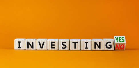 Investing yes or no symbol. Turned a wooden cube and changed words 'investing no' to 'investing yes'. Beautiful orange background. Business and investing yes or no concept, copy space.