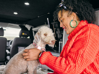 Woman sitting in back of van and playing with dog