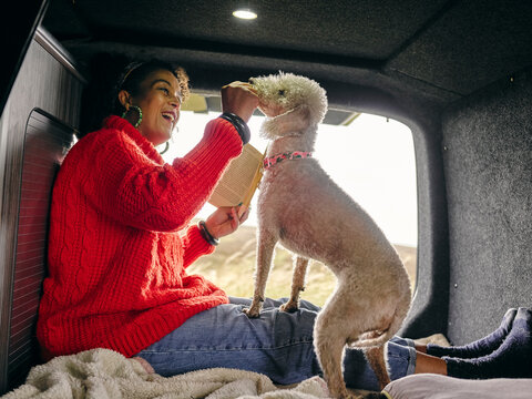 Woman sitting in back of van and playing with dog