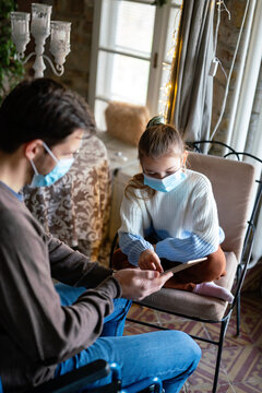 Father with disability in wheelchair using tablet at home with child while wearing masks.