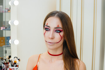 A young beautiful girl in a beautiful festive clown makeup for the Halloween holiday. Happy...