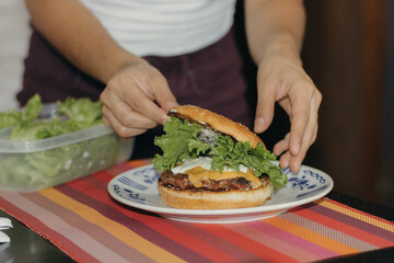 Hispanic young woman serving cheeseburger with lettuce on white plate