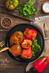 A plate with stuffed peppers and herbs on a wooden background. Hades from above, vertical.