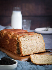 A loaf of soft fluffy organic bread bun earl grey tea perfume and leaves of tea inside, with slice pieces on a wooden board. Bottle of milk and plate in background. 