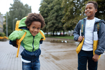 Little boys with back packs. Two African American boys next to the school. Back to the school concept. Kids standing outside and happy to meet each others. Happy black children. First day of school