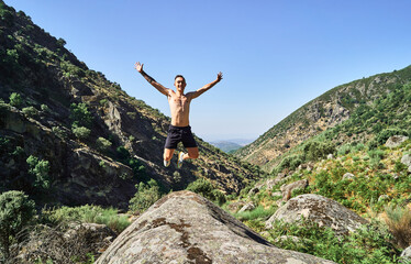 Young caucasian man, free and happy, jumping with open arms in a beautiful landscape with mountains