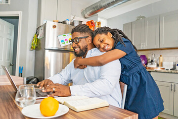 Girl hugging father working at home with laptop