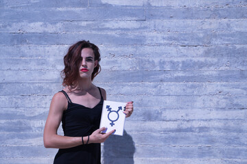 Young adult Hispanic transsexual girl pointing to her gender symbol on a notebook, on a gray cement...