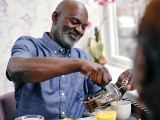 UK, SmilingÊman pouring coffee at breakfast table