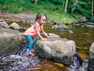 UK, Smiling girl playing in shallow creek - obrazy, fototapety, plakaty