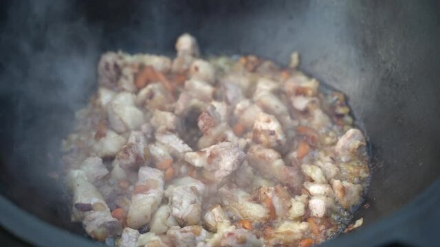 Meat and onions are stewed in a cauldron in a sauce close-up. Cooking pilaf in a cast-iron kazan, zirvak, oriental cuisine. Step 3 of 8