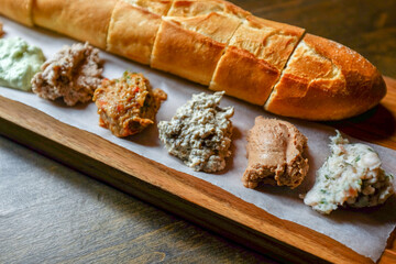 Various spreads on bread and fresh French baguette on a wooden table. Hearty breakfast. Blurred and...