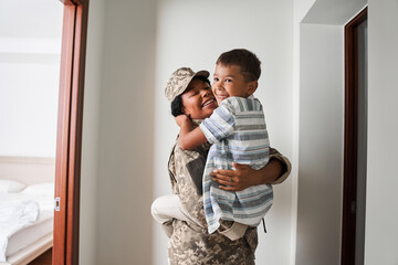 Black female soldier holds son on arms after army - obrazy, fototapety, plakaty