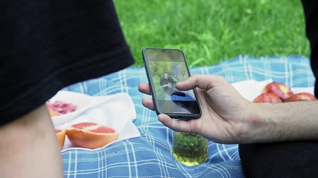 A man's hand holds a phone and flips through photos in nature in the summer