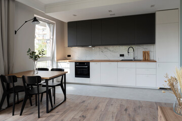 Modern kitchen interior with stylish furniture with wooden counter and marble on the wall. Contemporary dining room with table and chairs and window in new apartment.