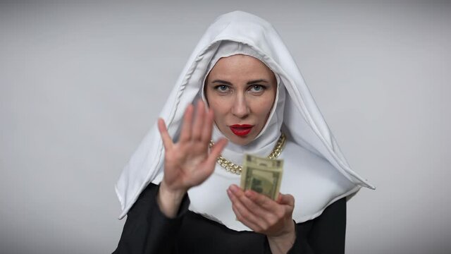 Gorgeous woman in nun costume scattering money in slow motion crossing hands looking at camera smiling. Portrait of provocative confident beautiful Caucasian lady posing at grey background