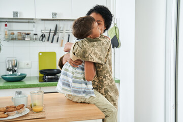 Black mother hugging her little son at kitchen